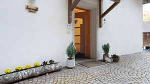 Ein Gebäudeeingang mit einer Holztür, einem Schild mit der Aufschrift 'SPRENG' und Blumentöpfen auf dem Kopfsteinpflaster.