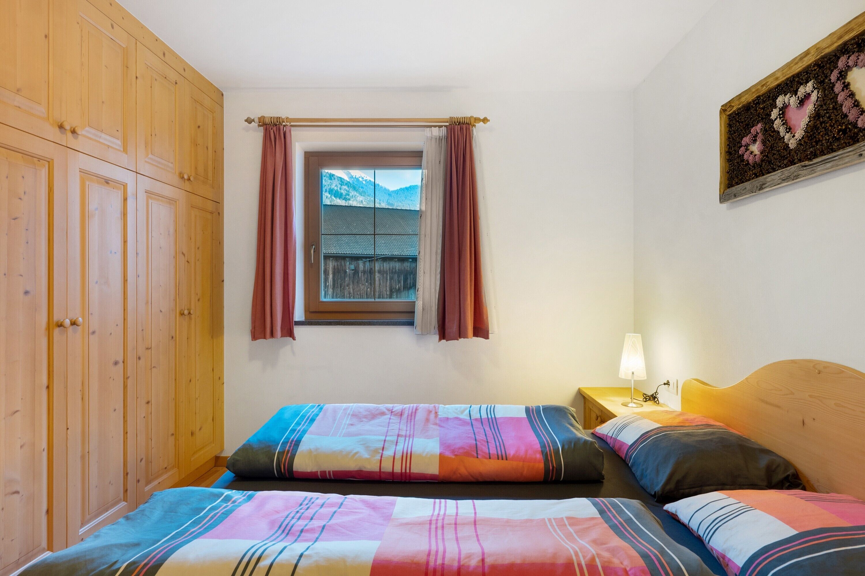 Une chambre avec deux lits, une armoire en bois, une fenêtre avec des rideaux et une lampe sur la table de chevet.