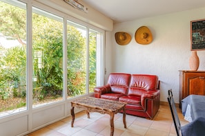 A room with a red leather sofa, a wooden coffee table, and a large window with a view of greenery.