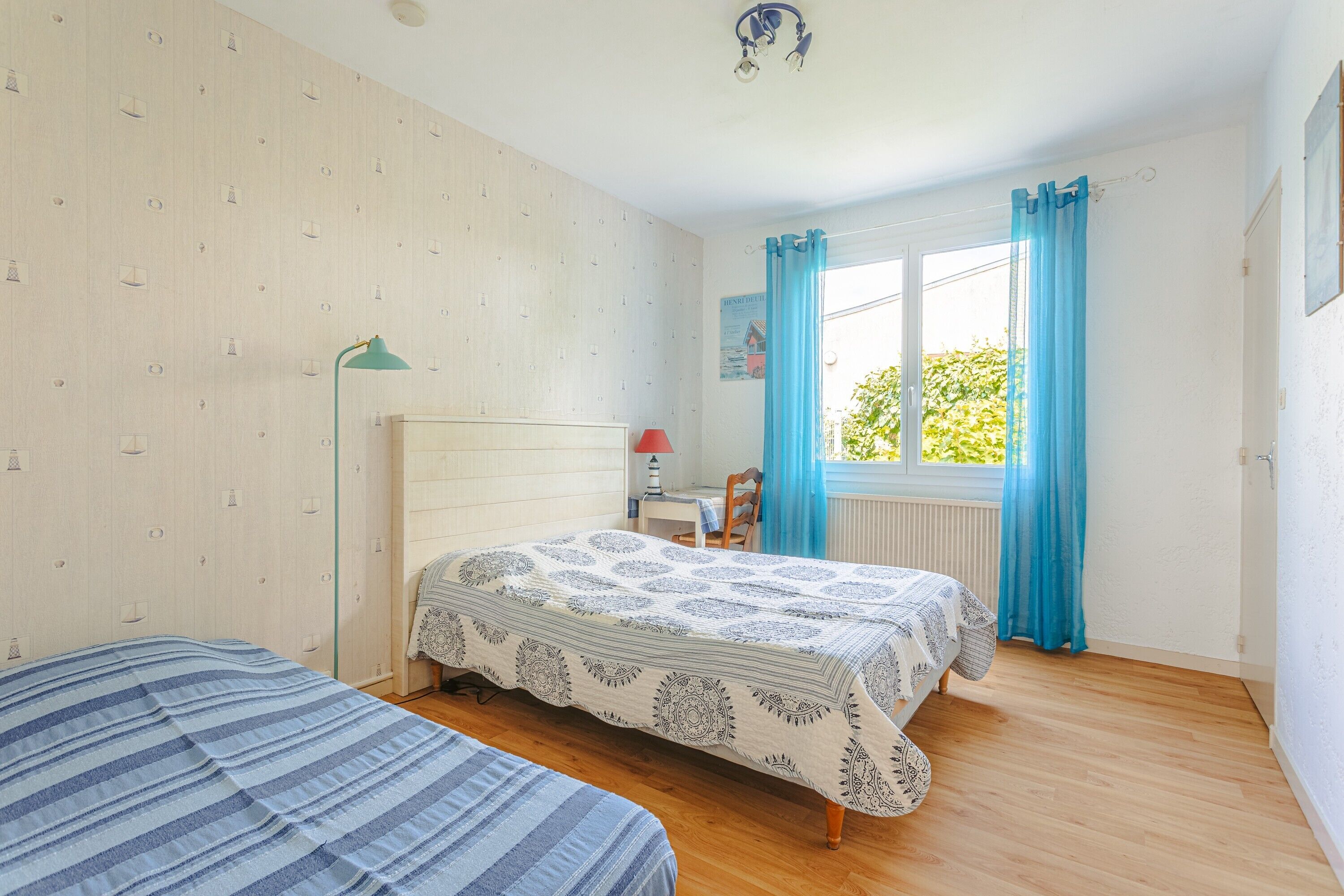 Un dormitorio con dos camas, un escritorio, una silla, una lámpara y una ventana con cortinas.