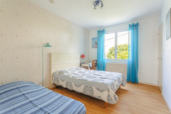 A bedroom with two beds, a desk, a chair, a lamp, and a window with curtains. - Bed and Breakfast 'Grillon La Brée Les Bains' with Shared Terrace, Shared Garden and Wi-Fi (La Brée-les-Bains)