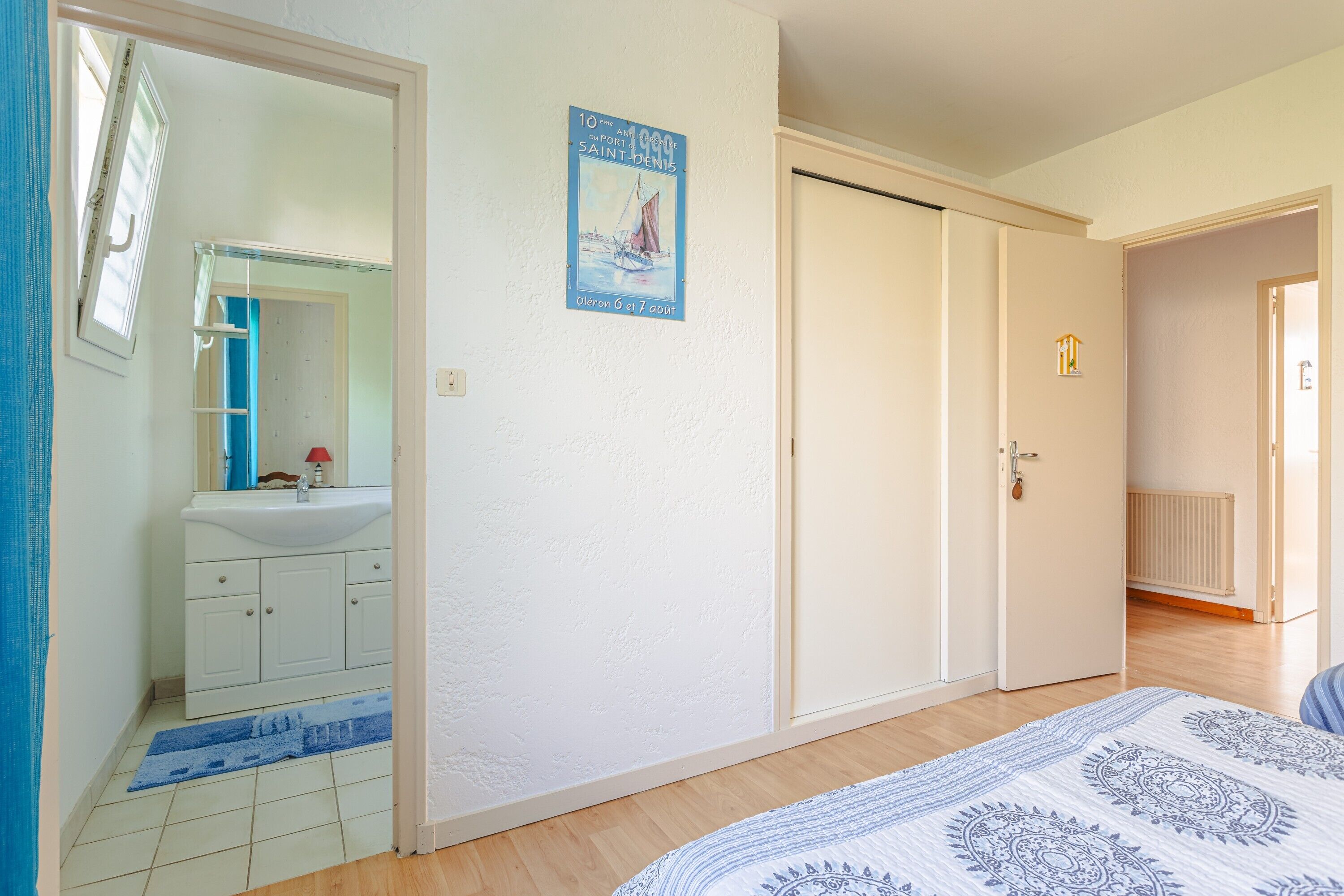 A bedroom with a bed, a white wardrobe, a bathroom with a sink and mirror, and a poster on the wall.