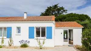 Un bâtiment blanc avec des volets bleus, un toit en tuiles et une allée gravillonnée.