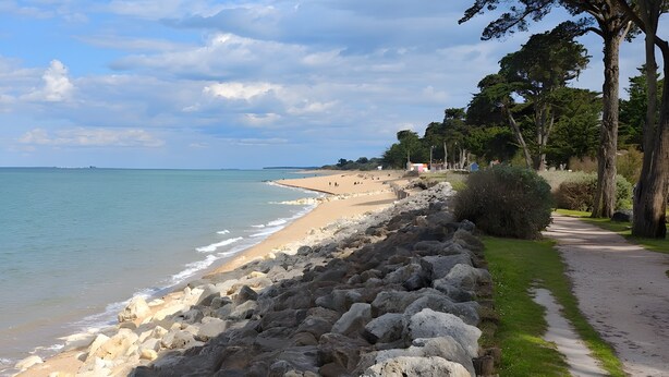 Ein Küstenpfad mit Felsbarriere, Strand und Bäumen.