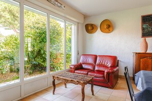 Una habitación con un sofá de cuero rojo, una mesa de centro de madera y un ventanal con vistas a la vegetación.