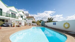 Piscina com deck revestido, boia na parede e edifício com fachada branca e detalhes verdes.