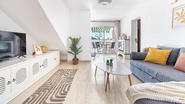 Uma sala de estar moderna com televisão, sofá, mesa de centro e vista para um pátio externo.