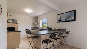 A modern kitchen with a central island, bar stools, a large window, and a sailboat painting. - Large family house in Fréhel | 8 guests | Ref 300 (FREHEL)