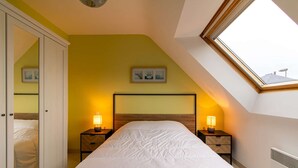 A bedroom with a sloped ceiling, a bed with white bedding, two bedside tables with lamps, and a skylight. - Large family house in Fréhel | 8 guests | Ref 300 (FREHEL)