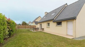 A residential property with a well-maintained lawn, a patio with outdoor furniture, and a single-story house with a sloped roof. - Large family house in Fréhel | 8 guests | Ref 300 (FREHEL)
