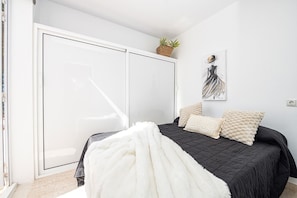 A bedroom with a bed, a white wardrobe, a plant, and a wall art piece.