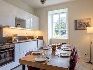 Une cuisine moderne avec des armoires blanches, un four encastré et un coin repas avec une table dressée pour quatre personnes.