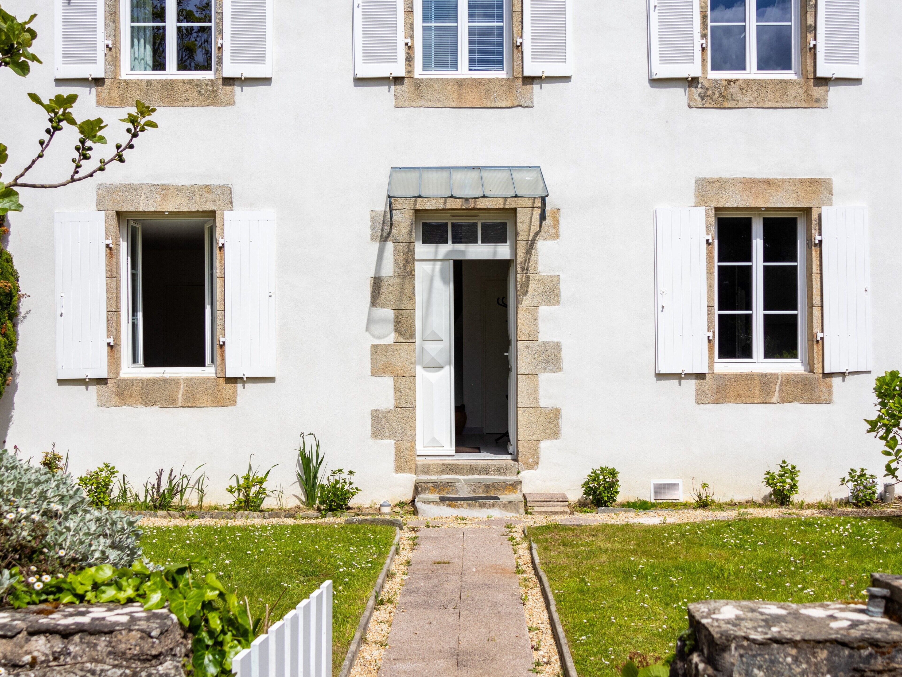 A white building with a central entrance, stone steps, and a small garden with a pathway leading to the door.