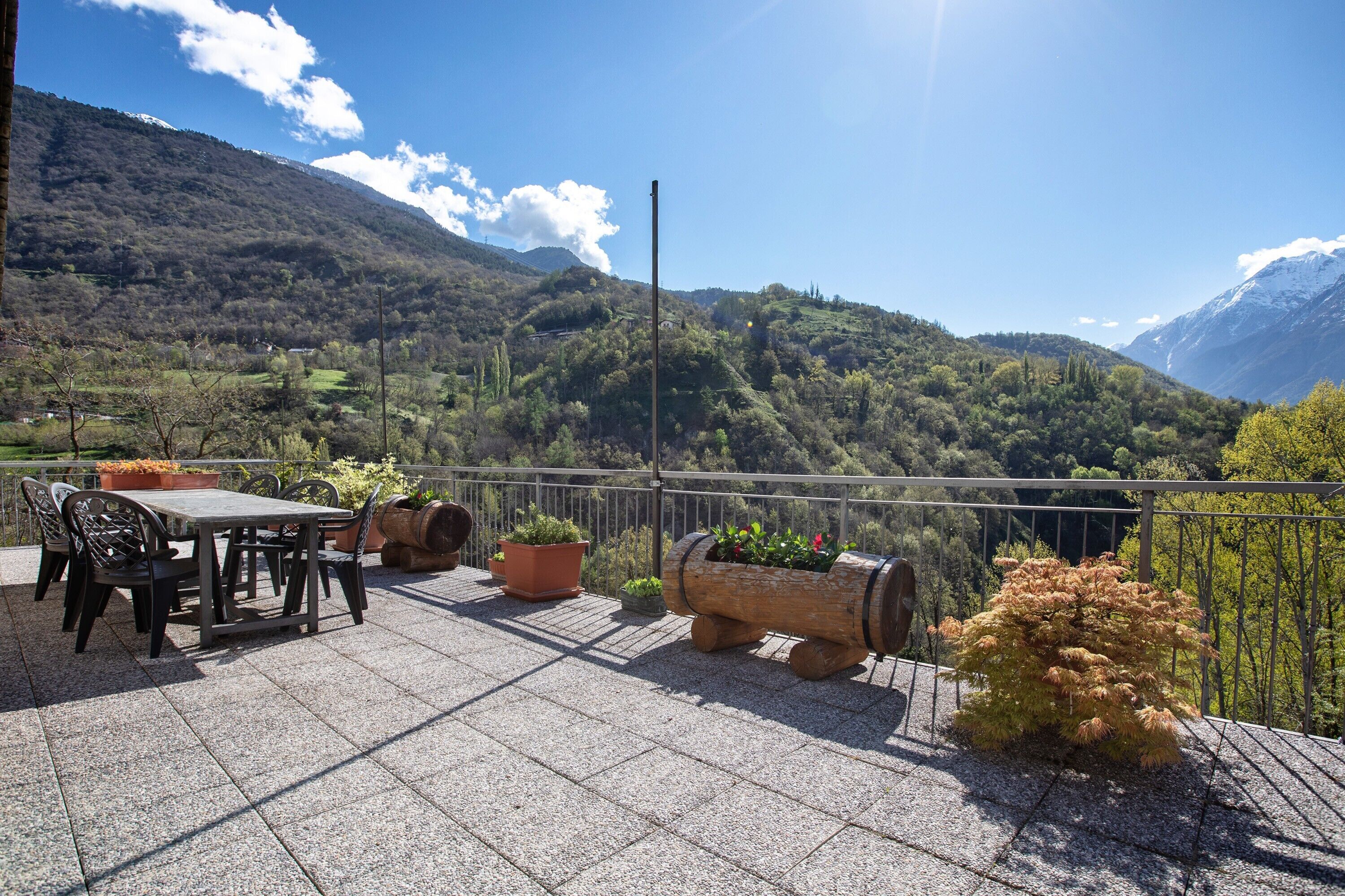 Una terraza con mesa y sillas, plantas en macetas y una vista panorámica de la montaña.