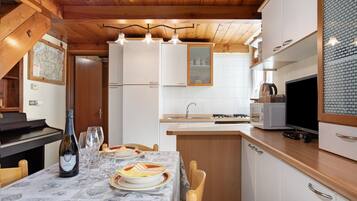 A kitchen with wooden cabinets, a dining table set for two, a wine bottle, and a television.