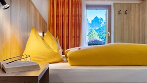 Ein Hotelzimmer mit Bett, Nachttisch mit Buch und Gläsern, Fenster mit Bergblick und Holzwänden.