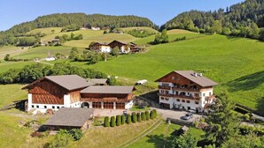 Ländliche Gegend mit traditionellen Holzbauten, ein großes zweistöckiges Gebäude mit Balkonen und einer gepflegten Rasenfläche.