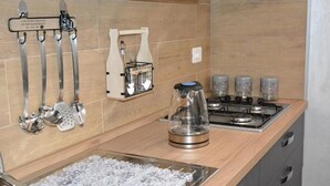 A kitchen with a stove, a kettle, and various utensils hanging on the wall.