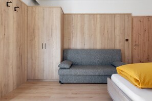 Una habitación con un sofá gris, un armario de madera y una cama con una manta amarilla.