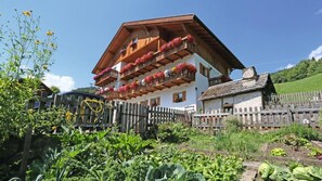 Een klassiek chalet met een houten balkon, versierd met bloemen, omgeven door weelderige begroeiing en een houten hek.