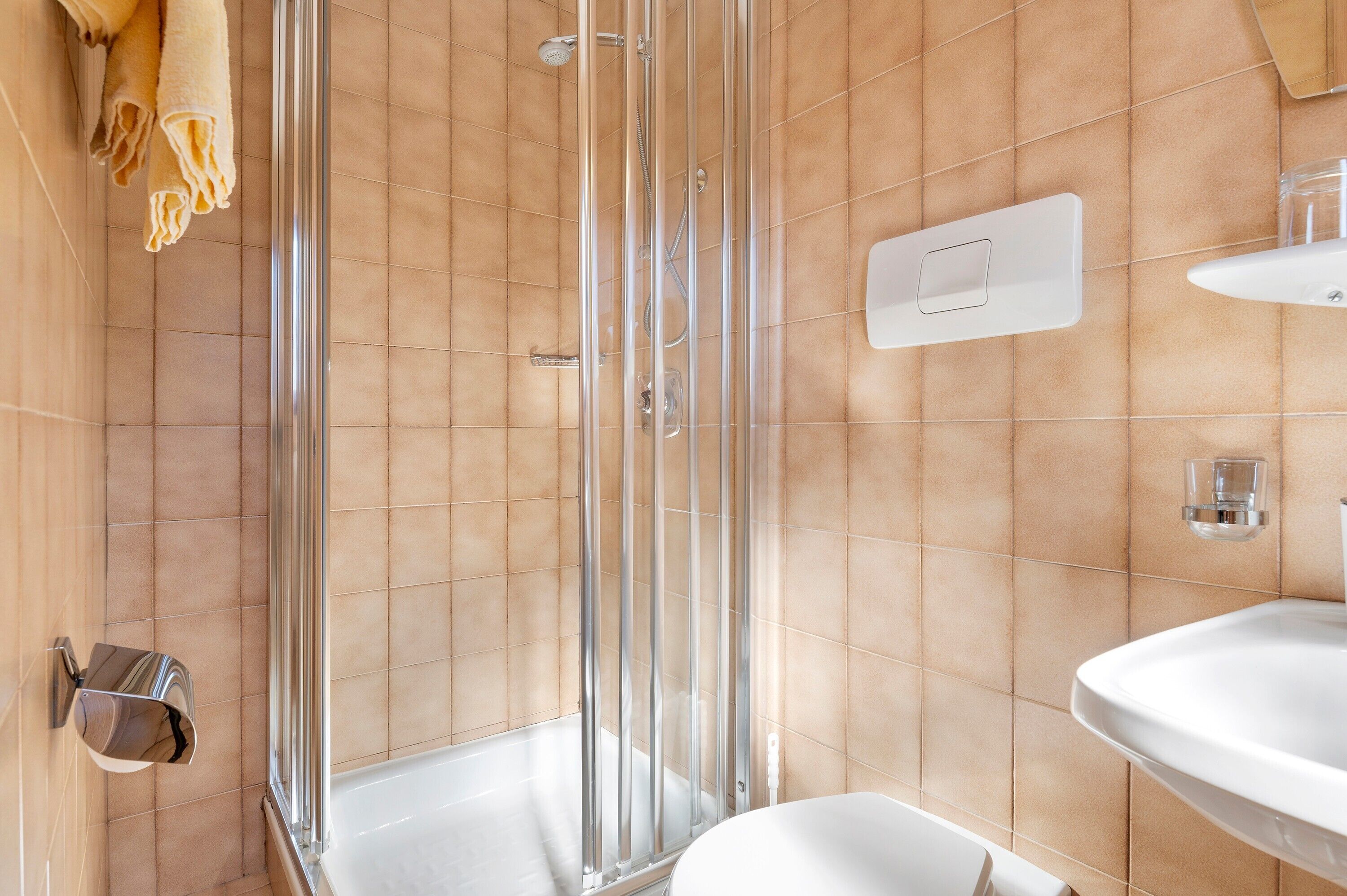Un baño con cabina de ducha de vidrio, un lavamanos blanco y un perchero para toallas.