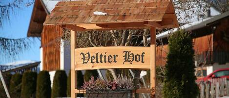 A wooden sign with the text 'Veltier Hof' and a planter with plants below it.