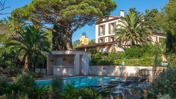 A pool area with lounge chairs, a large tree, and a building with a tiled roof. - Villa 'Chantegrive' with sea view, Wi-Fi and air conditioning (Roquebrune-sur-Argens)
