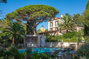 A pool area with lounge chairs, a large tree, and a building with a tiled roof. - Villa 'Chantegrive' with sea view, Wi-Fi and air conditioning (Roquebrune-sur-Argens)