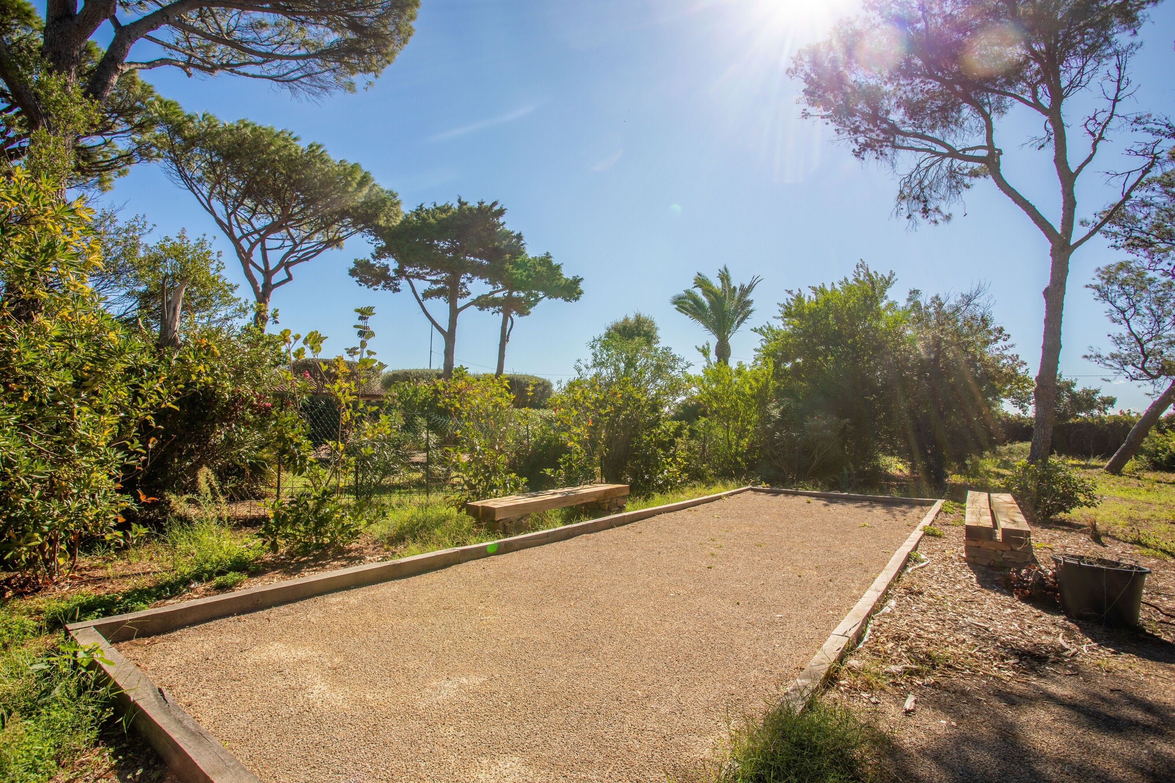 A gravel court with benches, surrounded by trees and greenery.