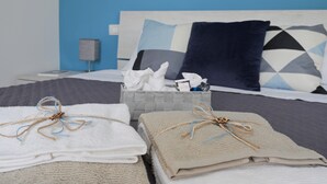 Ein ordentlich bezogenes Bett, eine blaue Wand, ein grauzwieliges Kissen und ein grauer Nachttisch mit einer Lampe.
