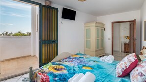 A room with a bed, a television, a wardrobe, and a door leading to a balcony.