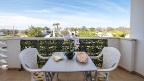 A balcony with two white plastic chairs, a small table, a potted orchid, and decorative plates.
