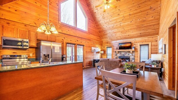 A spacious log cabin interior with a kitchen, dining area, and living room. - Unwind in the Hot Tub with Calming Treetop Vistas, Play Arcade Games & Sip Fireside - Wanderlust (Sevierville)