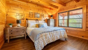 A cozy wooden cabin bedroom with a bed, nightstands, and a window with blinds. - Unwind in the Hot Tub with Calming Treetop Vistas, Play Arcade Games & Sip Fireside - Wanderlust (Sevierville)