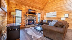 A cozy cabin interior with a stone fireplace, wooden walls, a sofa, and a coffee table. - Unwind in the Hot Tub with Calming Treetop Vistas, Play Arcade Games & Sip Fireside - Wanderlust (Sevierville)