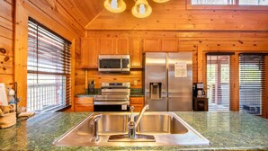 A kitchen with wooden walls, a stainless steel sink, a microwave, an oven, and a refrigerator. - Unwind in the Hot Tub with Calming Treetop Vistas, Play Arcade Games & Sip Fireside - Wanderlust (Sevierville)