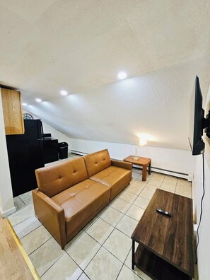 A modern living room with a brown leather sofa, a wooden coffee table, and a television mounted on the wall. - Nice apartment near Whole Foods, Brown University, Miriam Hospital, Downtown (Providence)