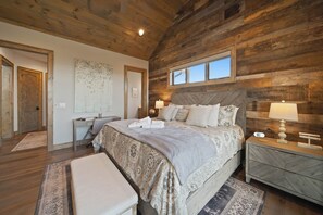 A bedroom with a large bed, two bedside tables with lamps, a desk, and a chair.