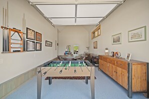 A room with a foosball table, a wooden cabinet with drawers, and framed pictures on the walls.