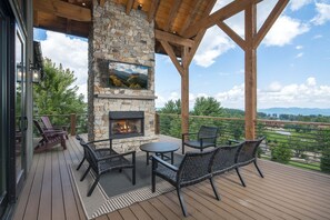 An outdoor deck with a stone fireplace, seating, and a TV mounted on the wall.