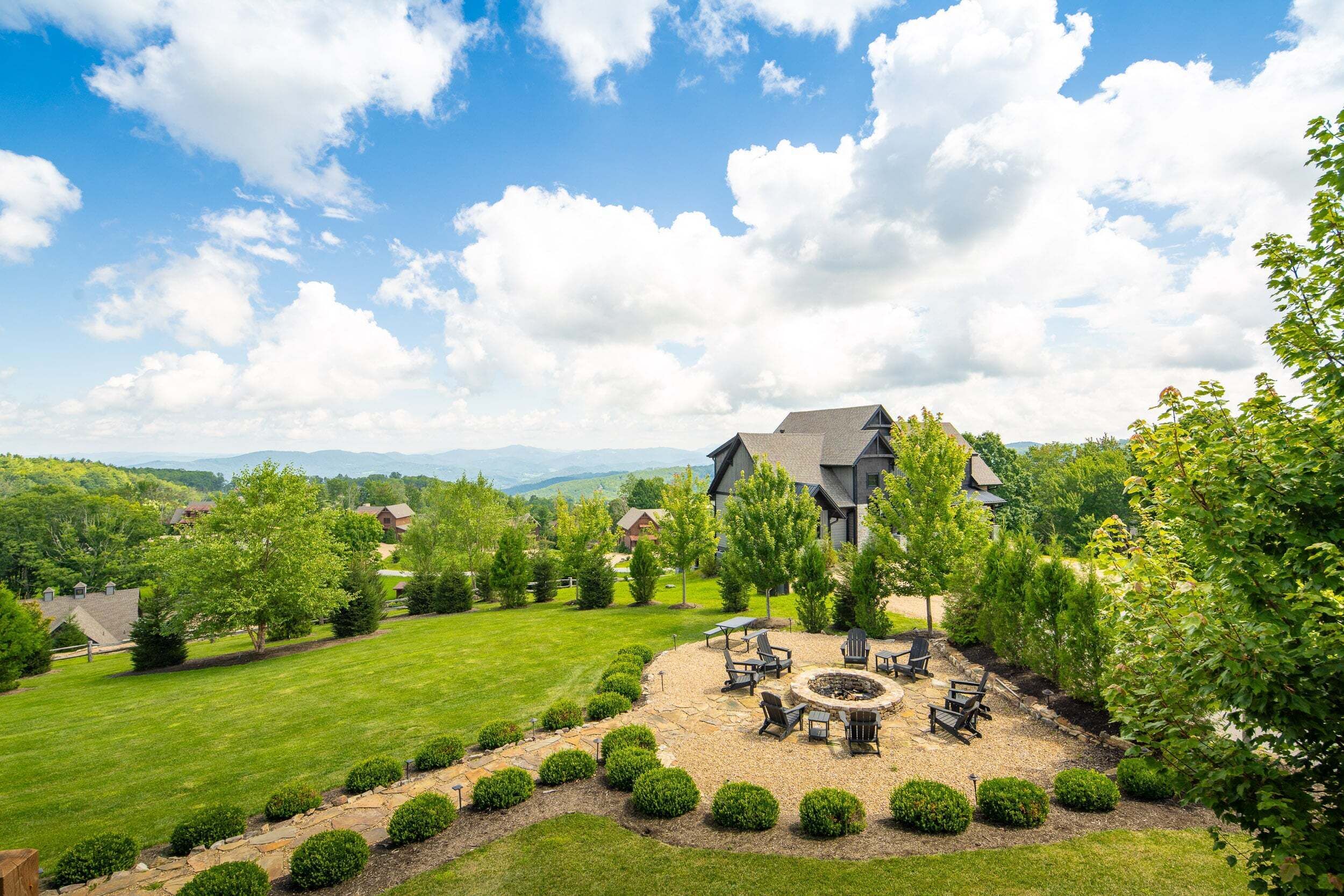 A large house with a well-maintained lawn and a fire pit area surrounded by chairs.