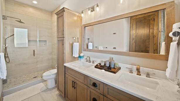 Une salle de bain moderne avec un grand miroir, un lavabo agrémenté d’un plateau de produits de toilette et un espace douche.