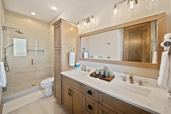 A modern bathroom with a large mirror, a sink with a tray of toiletries, and a shower area.
