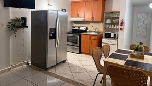 A modern kitchen with stainless steel appliances, wooden cabinets, and a dining area with wicker chairs. - Cozy 2-bedroom apartment in beautiful Yauco with AC, WiFi (Yauco)