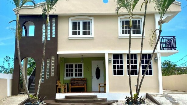 A two-story building with a balcony on the upper floor, a front door, and a staircase leading to the entrance. - Cozy 2-bedroom apartment in beautiful Yauco with AC, WiFi (Yauco)