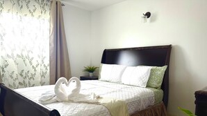 A neatly made bed with a heart-shaped towel arrangement, a dark wooden headboard, and a small potted plant on the nightstand. - Cozy 2-bedroom apartment in beautiful Yauco with AC, WiFi (Yauco)
