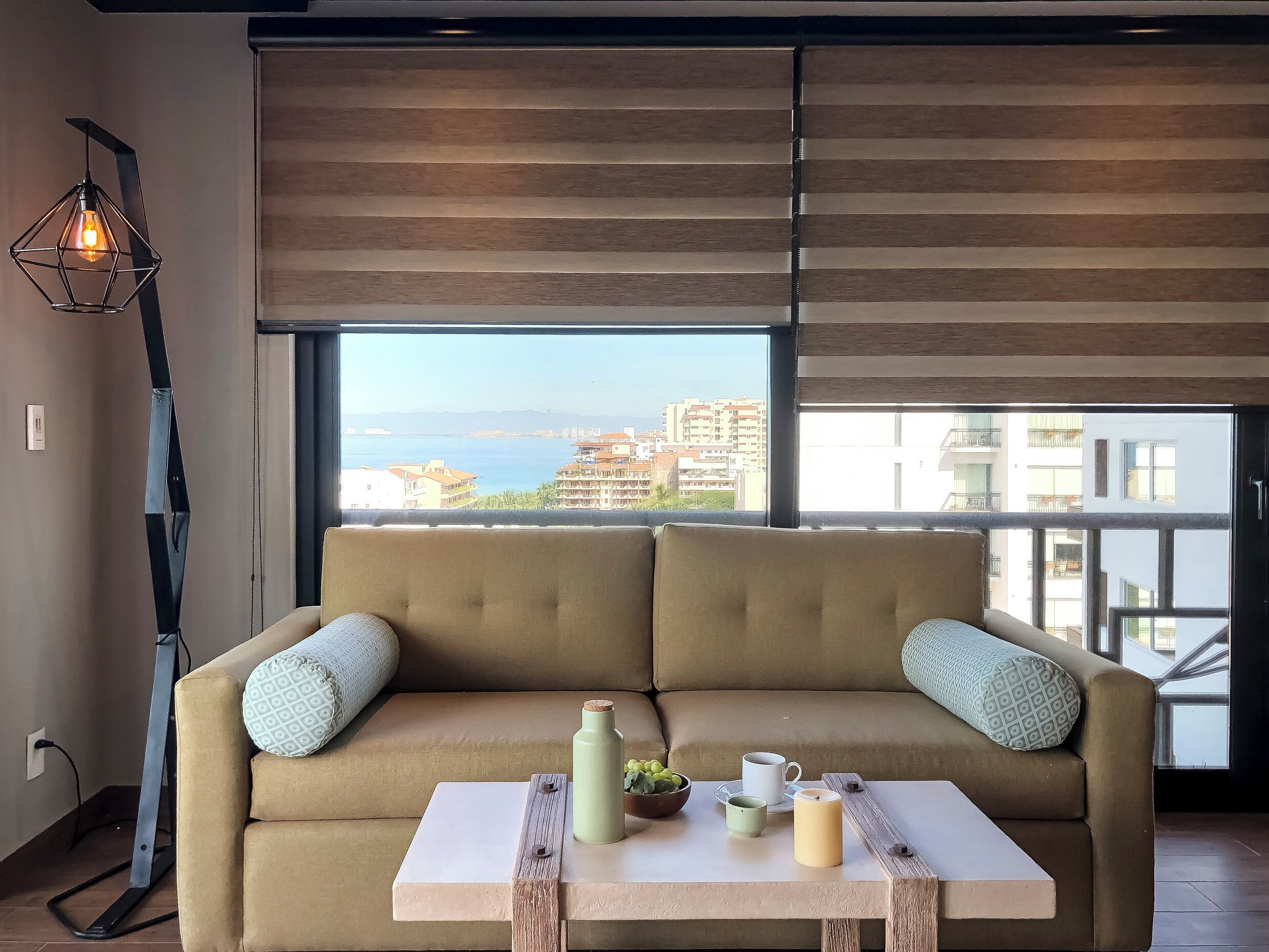 Sala de estar moderna com sofá bege, mesa de centro e vista para o mar e edifícios.