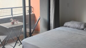 A bedroom with a bed, a small table with chairs, and a view of the outside balcony. - Charming studio next to PUC-SP, Allianz Parque and Pacaembu (Perdizes São Paulo)