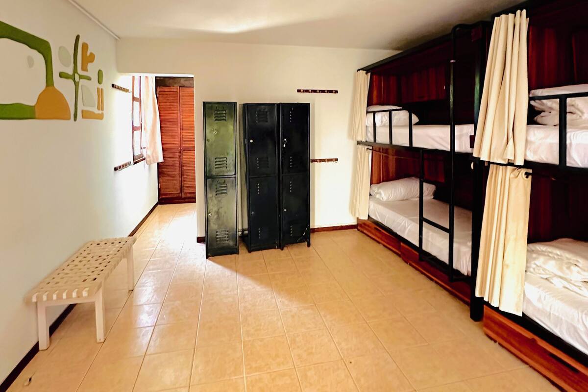 A dormitory room with bunk beds, a bench, lockers, and a hanging light fixture.