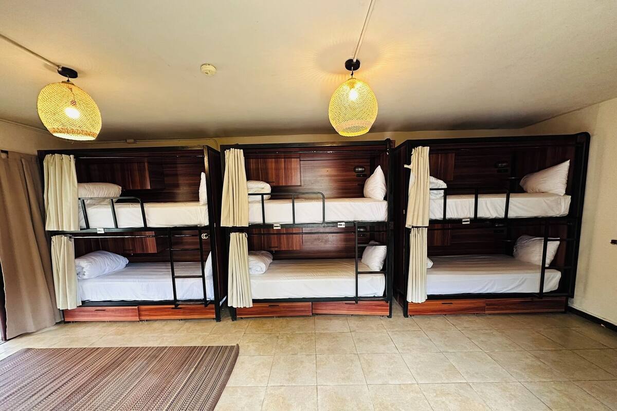 A room with three bunk beds, a wooden floor, and two hanging lamps.